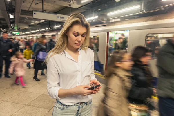 Jeune femme tapant sur le téléphone intelligent à la station de métro — Photo