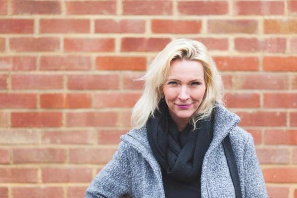 Portret van een blonde vrouw met bakstenen muur achtergrond — Stockfoto