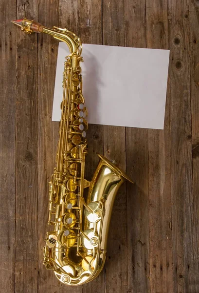 elegant classic musical instrument bronze saxophone on old wooden background with sheet of blank paper with place for text