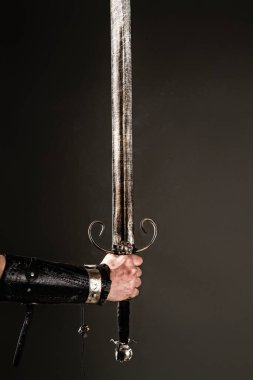 Kara arka planda büyük bir şövalye kılıcı tutan zırhlı bir adam.