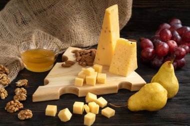 Tahta kesme tahtasındaki çeşitli peynir, armut ve fındık çeşitleri.