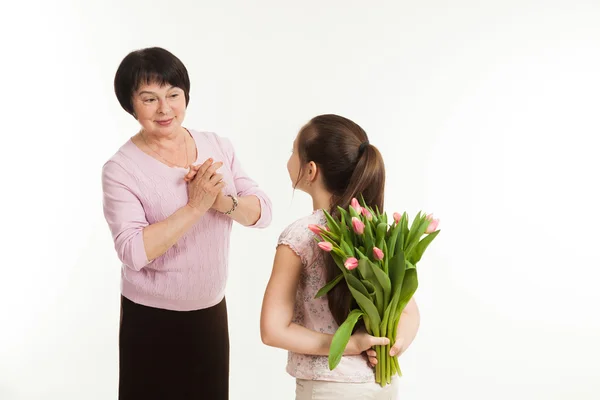 The granddaughter hides a bouquet of flowers for the grandmother — Stock Photo, Image