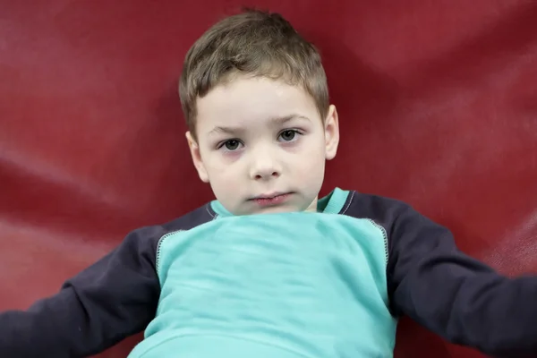 Niño en un sofá rojo — Foto de Stock