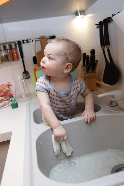 Baby boy sitting in the kitchen sink — Stock Photo, Image