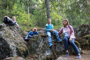 Anne ve oğulları ormanda taşın üzerinde oturuyorlar, Karelia.
