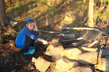 Çocuk ormanda ateşte sosis kızartıyor, Karelia.