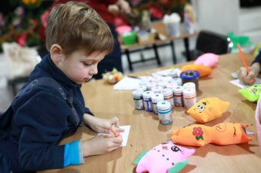 Atölyede kağıt üzerine yumuşak oyuncak tasarımı çizen çocuk