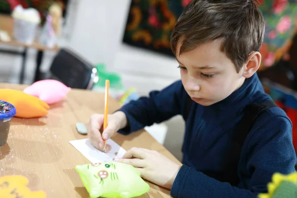 ワークショップで紙に柔らかいおもちゃのデザインを描く男の子 — ストック写真