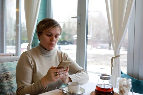 在咖啡馆里拿着智能手机和茶的女人的画像 — 图库照片