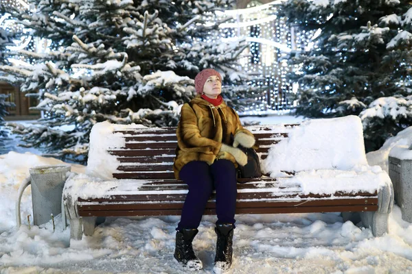 女人晚上坐在雪地的长椅上 — 图库照片