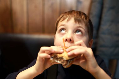 Restoranda hamburger yiyen çocuğun portresi.
