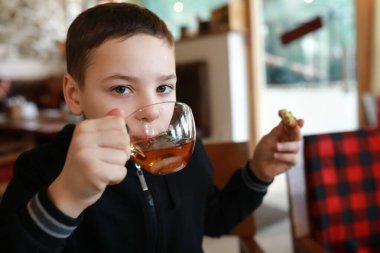 Çocuk lokantada çörekle çay içiyor.