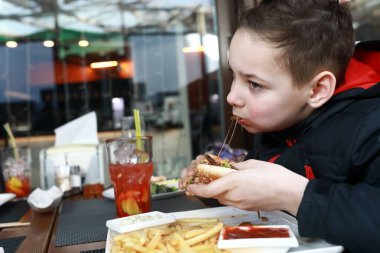 Baharda restoranın terasında hamburger yiyen çocuk.