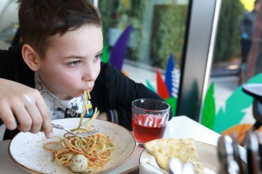Restoranda tavuk köfteli spagetti yiyen çocuk.