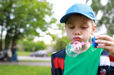 Çocuk parkta sabun köpüğü üflüyor.