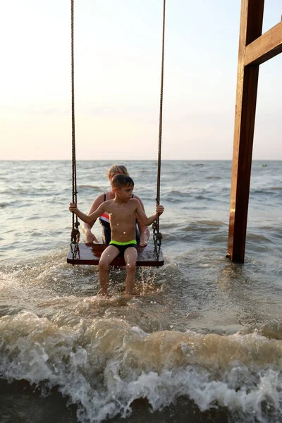 日没時にアゾフ海でスイング上の女性岩の少年 — ストック写真