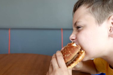 Aç çocuk bir restoranda hamburger yiyor.
