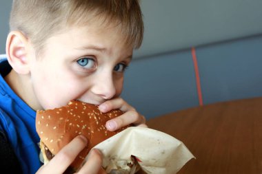 Aç çocuk lokantada hamburger yiyor.