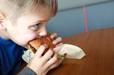 Restoranda hamburger yiyen aç bir çocuk.