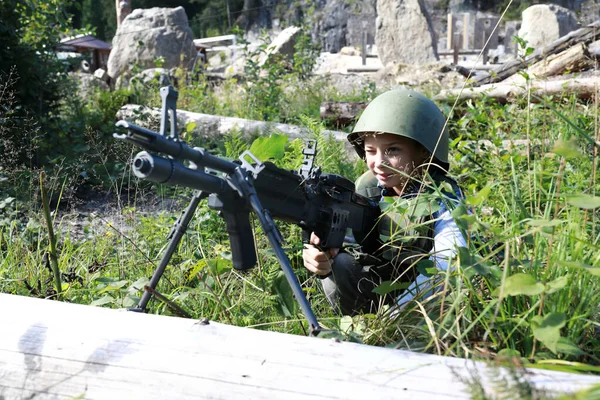 Askeri kasklı çocuk parkta makineli tüfekle ateş ediyor.