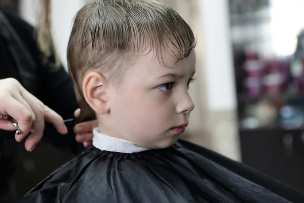 Парикмахер стрижет волосы серьезного ребенка — стоковое фото