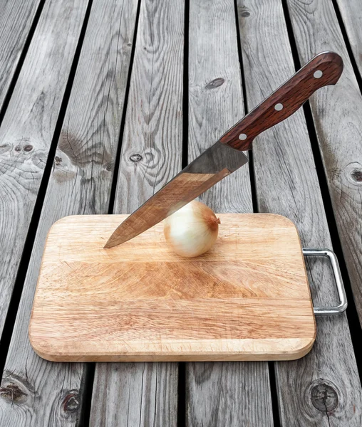 Cuchillo, cebolla y tabla de cortar sobre mesa de madera — Foto de Stock
