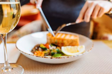 Kızarmış sebzeli somon bifteği yiyen kadın.