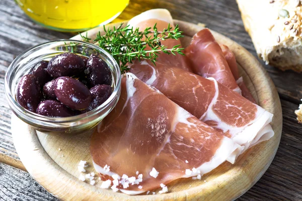 Thin slices of prosciutto with olives — Stock Photo, Image