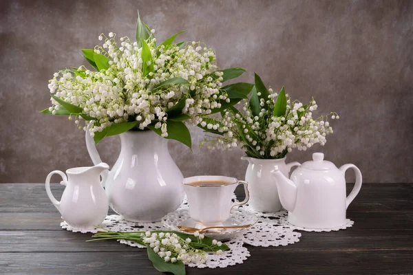 Desayuno romántico, té y lirios del valle en un jarrón sobre una mesa vieja — Foto de Stock