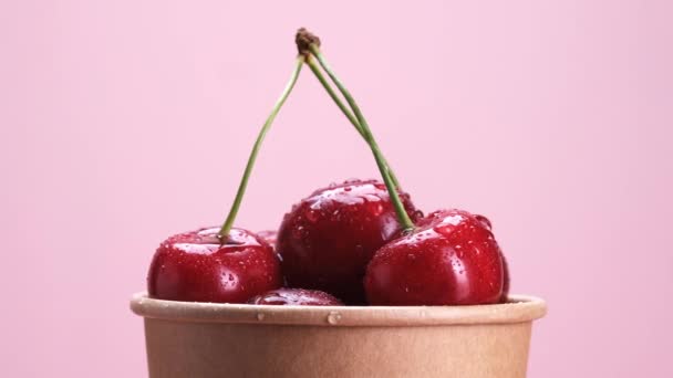 Cerezas Maduras Una Taza Cartón Ecológico Rotar Sobre Fondo Rosa — Vídeos de Stock