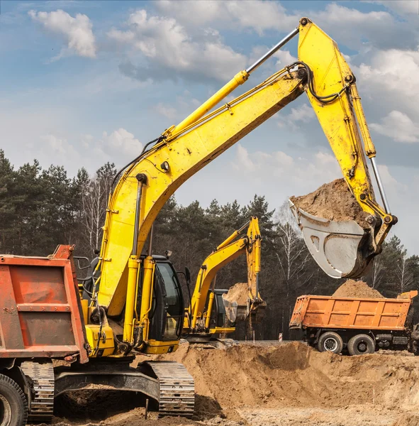 Bagger verschiffen Sand in Lastwagen auf Straßenbaustelle — Stockfoto