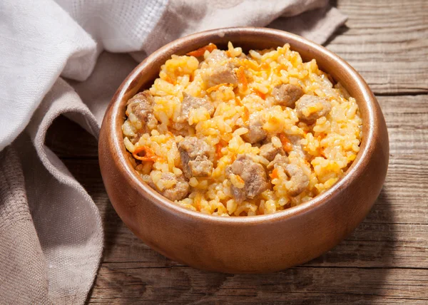 A delicious pilaf in a dish on the old board — Stock Photo, Image
