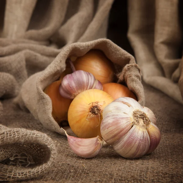 Zwiebeln und Knoblauch in einem Beutel groben Tuchs auf dem Tisch — Stockfoto