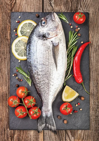 Свежая рыба, лимон, специи и помидоры черри на каменной доске — стоковое фото