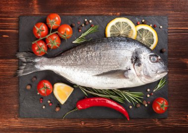 Taze balık, limon, baharat ve bir tahta üzerinde domates