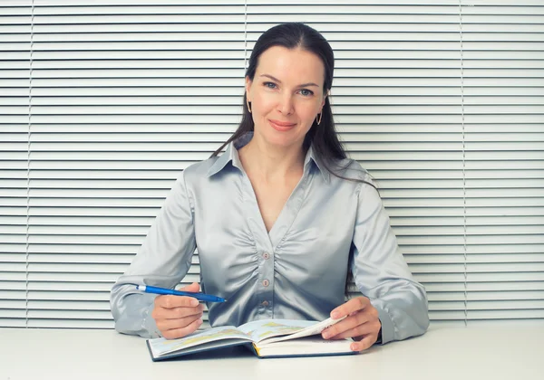 Usměvavá brunetka žena sedící na kancelářský stůl — Stock fotografie