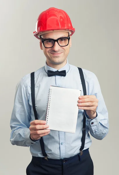 Homem de negócios em um capacete mostra a folha em branco do bloco de notas — Fotografia de Stock