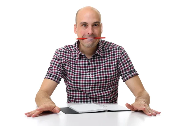 Bald man sitting at desk with pencil in his mouth — Stock Photo, Image