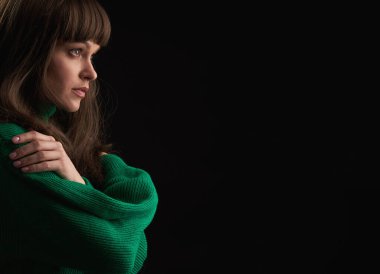 Uzun kahverengi saçlı güzel bir kadın siyah arka planda yeşil örülü süveter giyiyor. Stüdyo çekimi