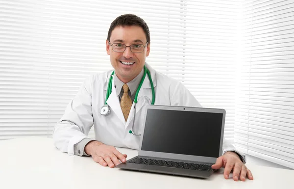 Доктор сидит за своим столом с ноутбуком Лицензионные Стоковые Фото