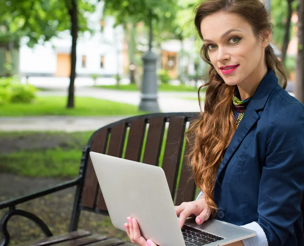 Νεαρή γυναίκα κάθεται στον πάγκο με το laptop — Φωτογραφία Αρχείου
