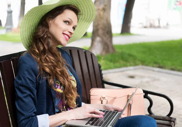 Giovane donna seduta sulla panchina con computer portatile — Foto Stock