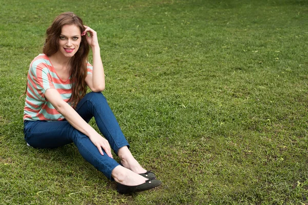 Jovem mulher sentada em uma grama — Fotografia de Stock