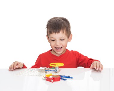 The five-year-old boy sits at a white table and plays an electronic designer clipart
