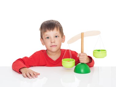The five-year-old boy sits at a white table and plays with wooden scales clipart