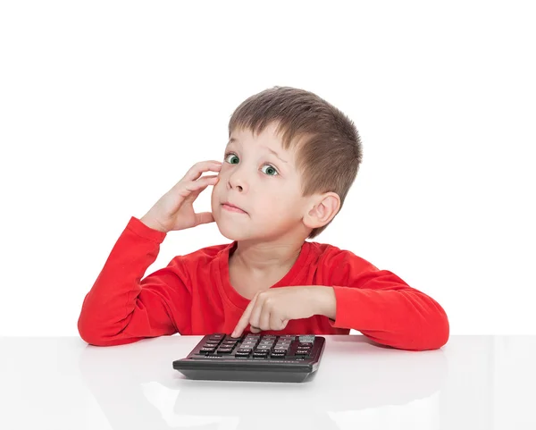 П'ятирічний хлопчик сидить за білим столом і натискає на кнопку калькулятора — стокове фото