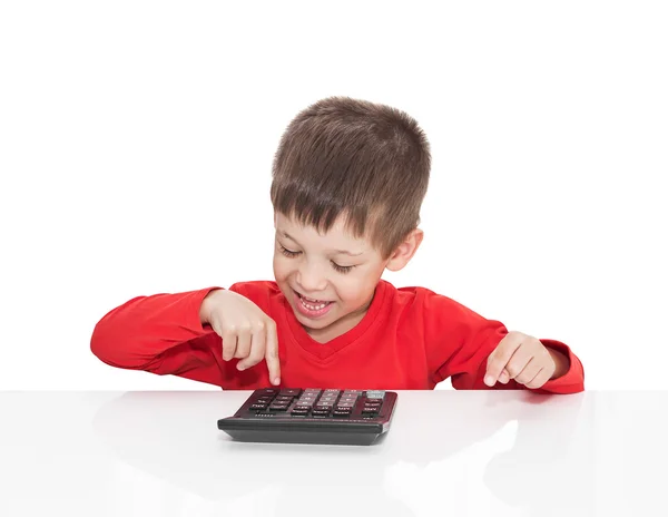 O menino de cinco anos sentado em uma mesa branca e pressiona a calculadora de botão — Fotografia de Stock