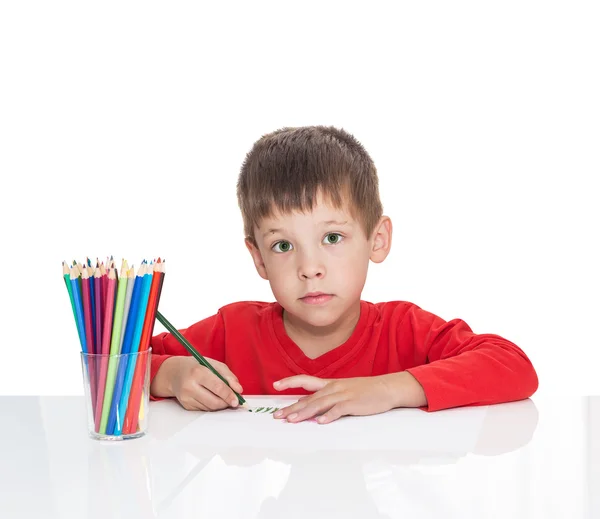 П'ятирічний хлопчик сидить за білим столом і малює олівці — стокове фото