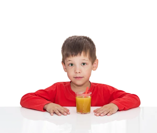 П'ятирічний хлопчик сидить за білим столом біля апельсинового соку з соломи — стокове фото
