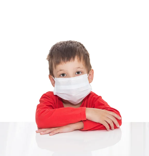 De zieke vijf-jaar-oude jongen zit aan een witte tafel met geneeskunde gezondheidszorg masker — Stockfoto